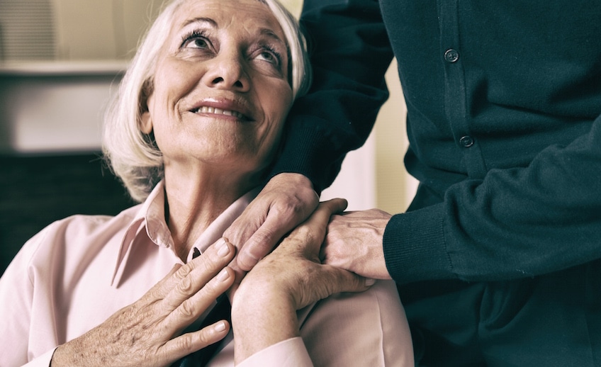 Senior woman on wheelchair taking her husband’s hand